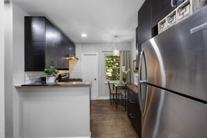 A modern kitchen with dark cabinets, a stainless steel refrigerator, and a small island with a plant. - MIMO5-5 | cozy corner of Miami's Modern District (Miami)