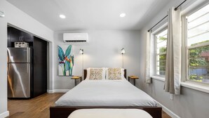 Une chambre moderne avec un lit, des tables de chevet, un appareil de climatisation et une fenêtre avec des rideaux.