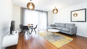 A modern living room with a grey sofa, a round coffee table, a dining area with chairs and a table, and two pendant lights. - Fernbank by Dublin At Home (Dublin 14)