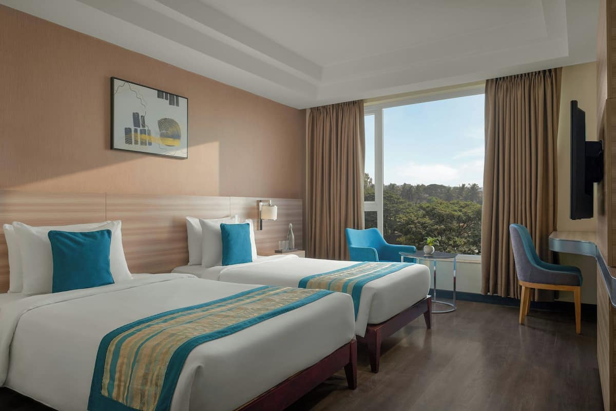 A hotel room with two beds, a desk, a chair, and a large window with curtains.