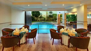 Comedor con mesas dispuestas para cuatro, con vistas a una piscina.
