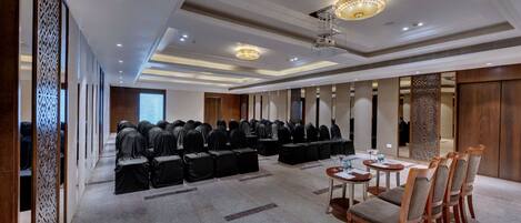 A conference room with rows of chairs and tables, a patterned wall divider, and a chandelier.