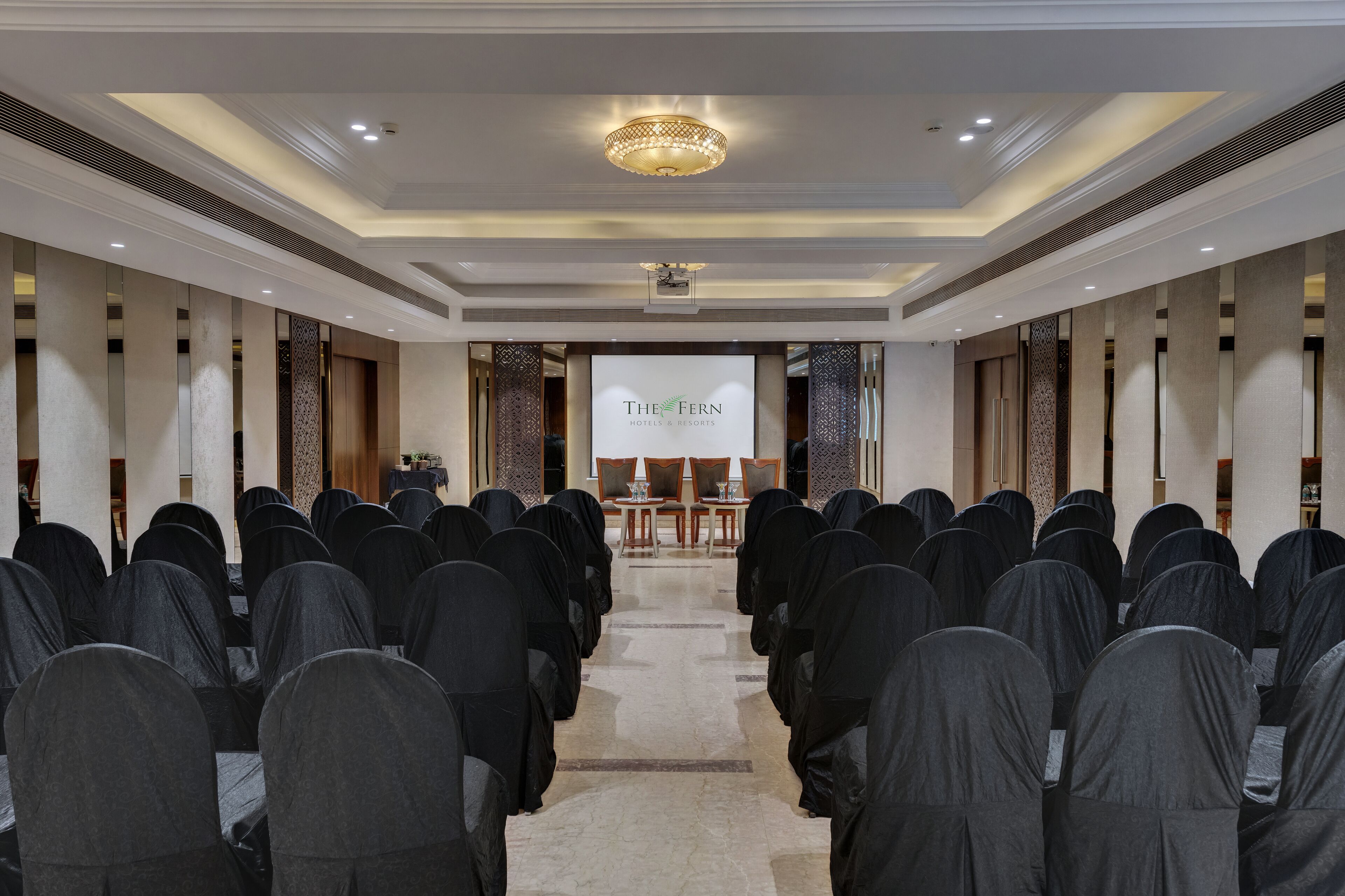 Una sala conferenze con file di sedie, un podio e un grande schermo che mostra 'The Fern Hotels & Resorts'.