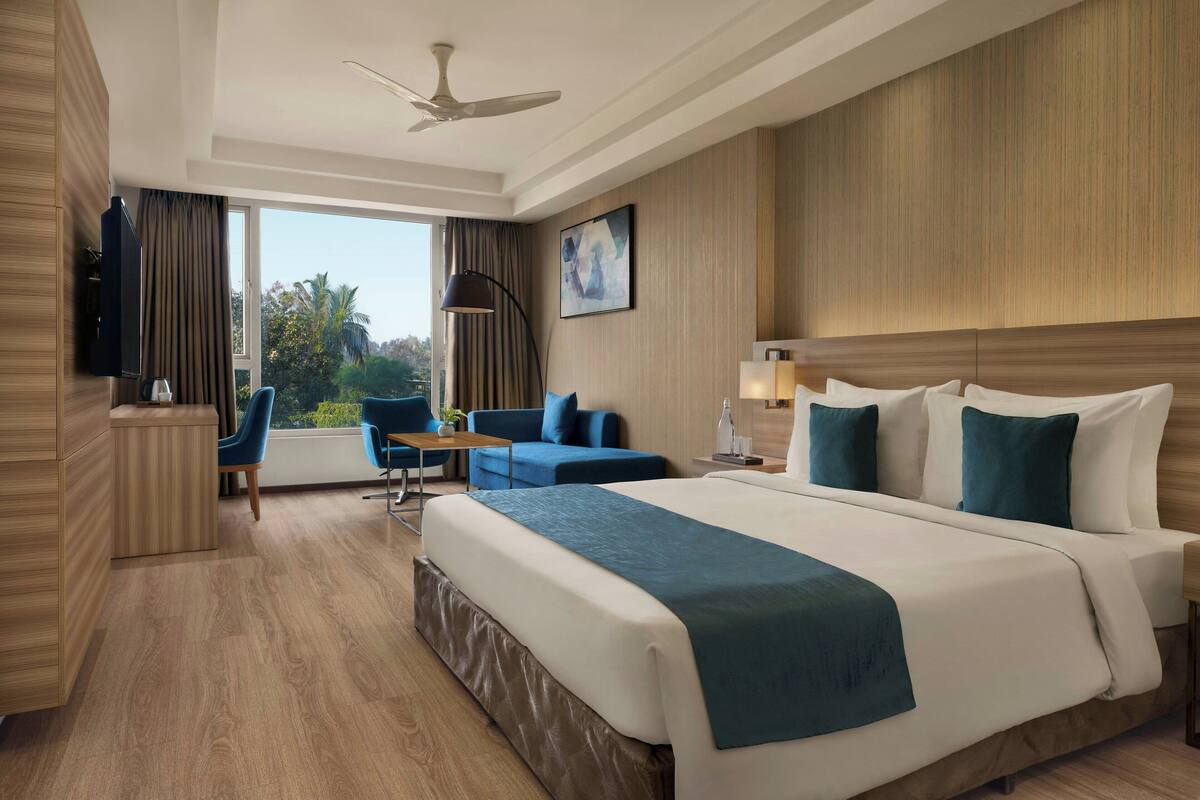 A hotel room with a large bed, a desk, a chair, a TV, and a window with curtains.