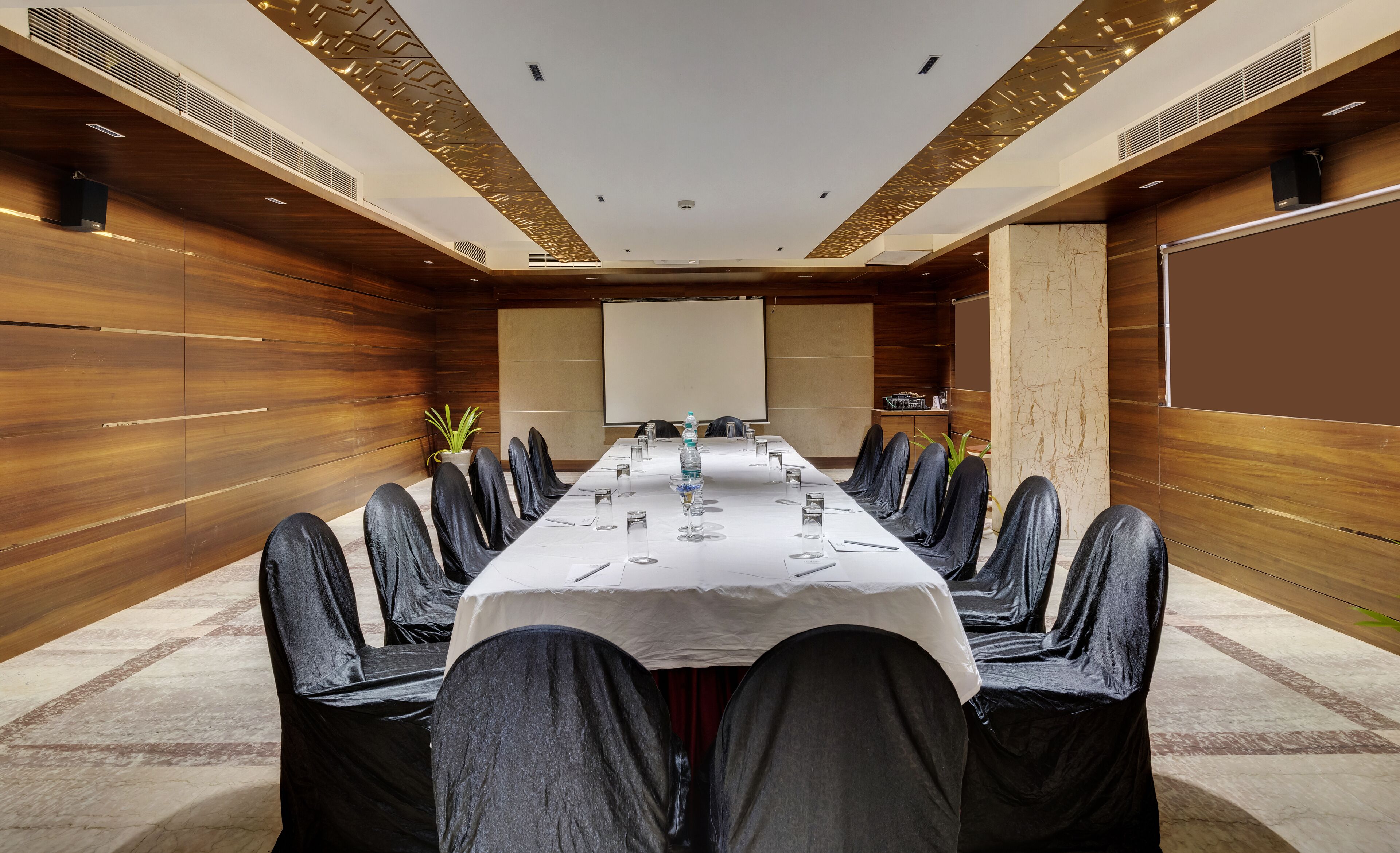 A conference room with a long table, black chairs, and a projector screen.