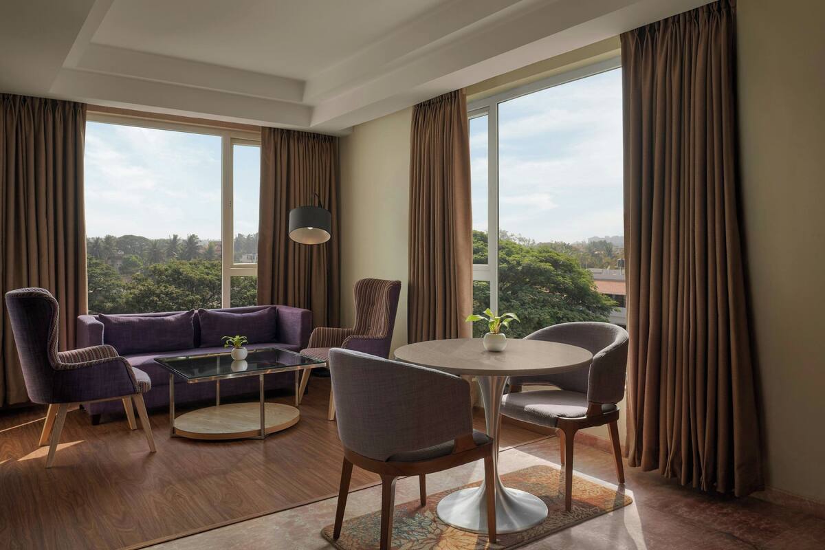 A modern hotel room with a large window, a purple sofa, a round dining table, and a chair.