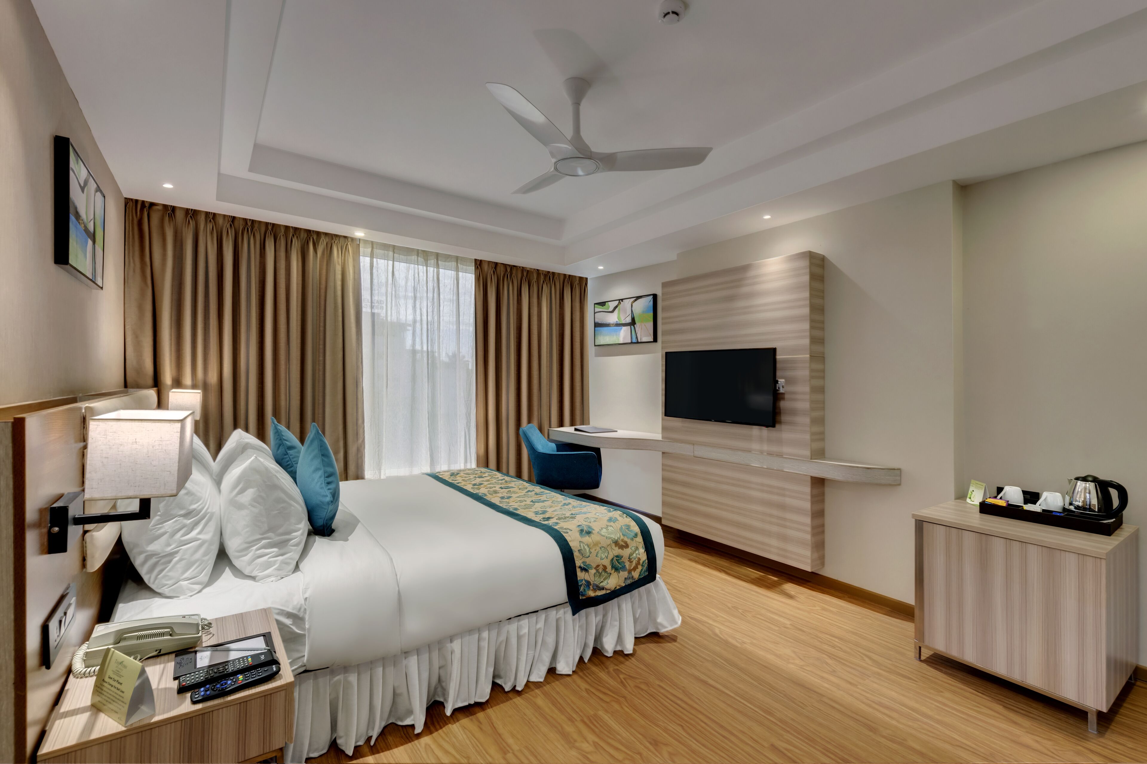 A hotel room with a bed, bedside table, lamp, desk, chair, TV, and a small cabinet.