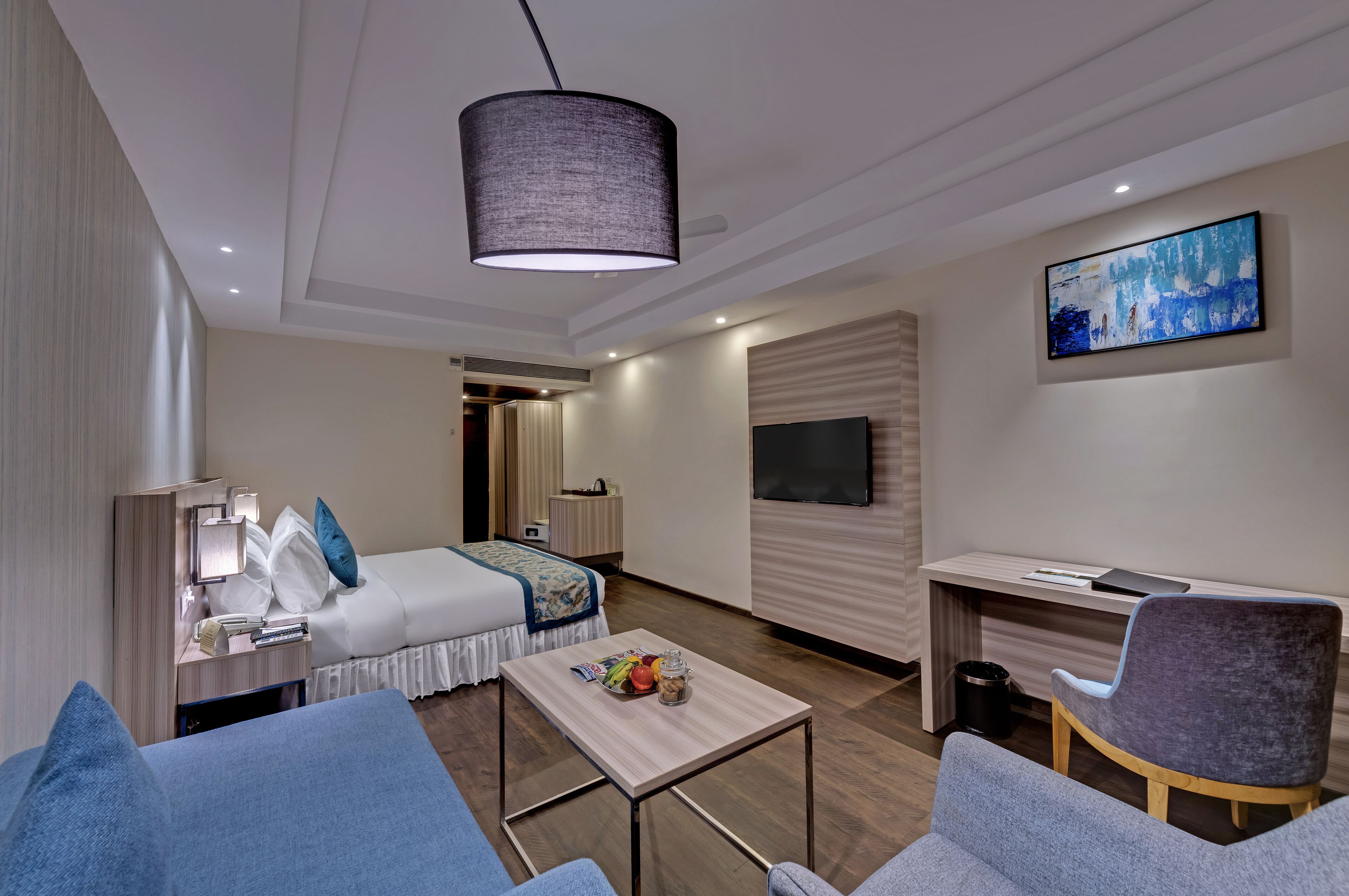 Ett modernt hotellrum med en säng, ett skrivbord, en TV och en sittgrupp.