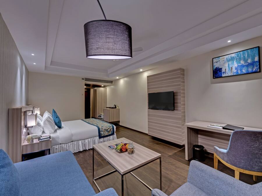 A modern hotel room with a bed, a desk, a TV, and a seating area.