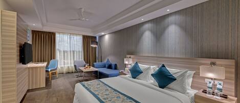 Habitación de hotel con una cama grande, un escritorio, una silla, un televisor y una ventana con cortinas.