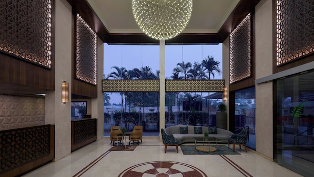 Un vestíbulo amplio con un gran diseño circular en el suelo, zona de estar con sofás y sillones, paneles decorativos en la pared y grandes ventanales con vistas a palmeras.