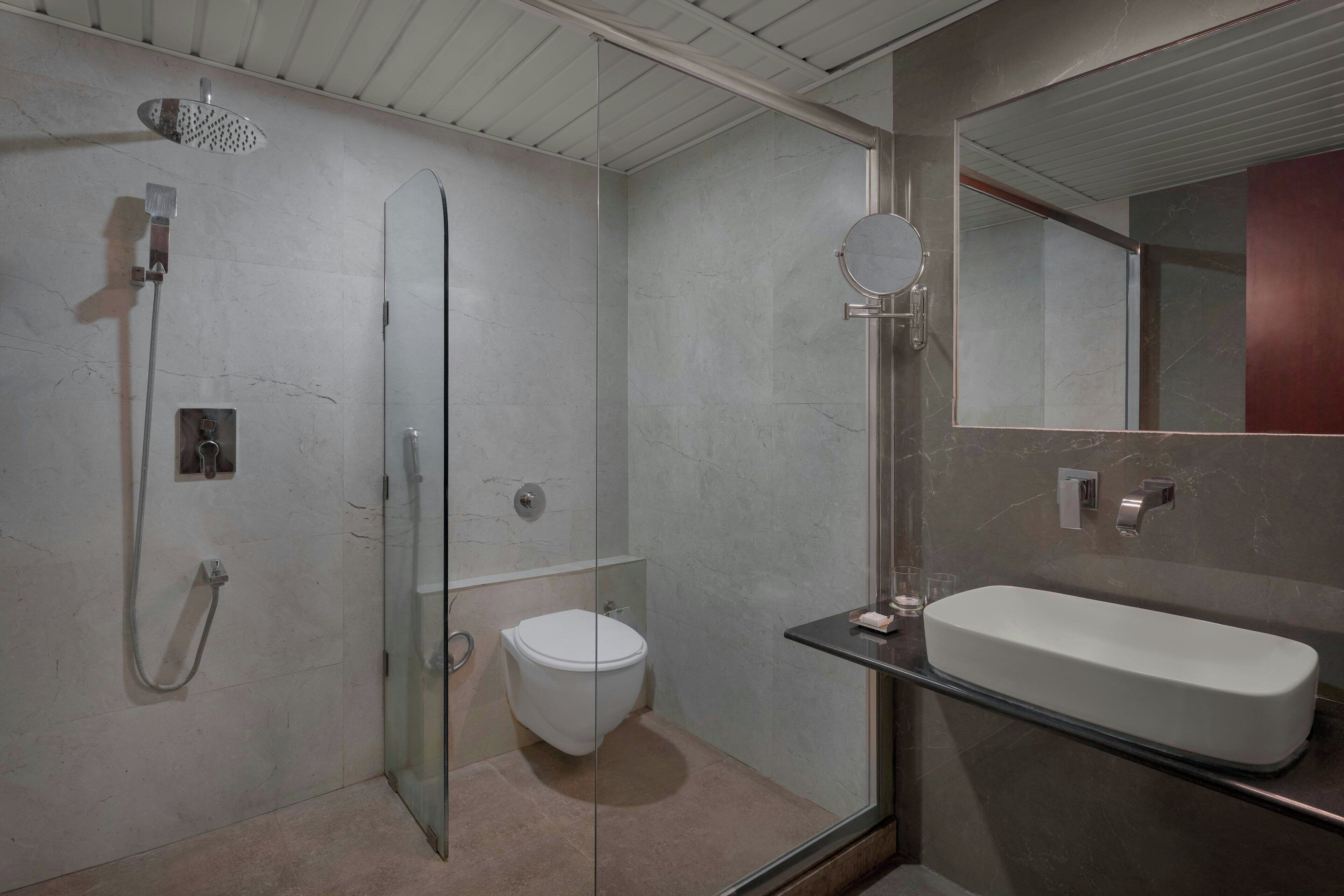 Un baño moderno con cabina de ducha de vidrio, inodoro y un espejo grande sobre un lavabo rectangular.