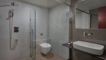 Un baño moderno con cabina de ducha de vidrio, inodoro y un espejo grande sobre un lavabo rectangular.