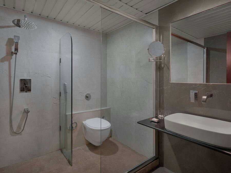Un baño moderno con cabina de ducha de vidrio, inodoro y un espejo grande sobre un lavabo rectangular.