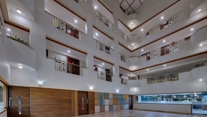 Un vestíbulo de hotel con varios niveles, un atrio central, paneles de madera y una vitrina de vidrio.