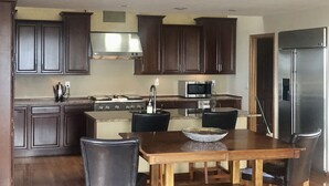 A kitchen with dark wooden cabinets, a stainless steel range hood, a microwave, a refrigerator, and a dining table with four chairs.