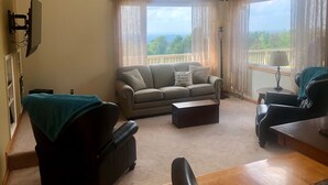 Ein Wohnzimmer mit einer Couch, Sesseln, einem Couchtisch, einem an der Wand montierten Fernseher und einem Balkon mit Blick.
