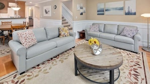 A living room with two grey sofas, a round coffee table with a vase of sunflowers, and a patterned rug. - Perch - Cozy Ensuites: 3BR/3BA townhome with parking (Seattle)