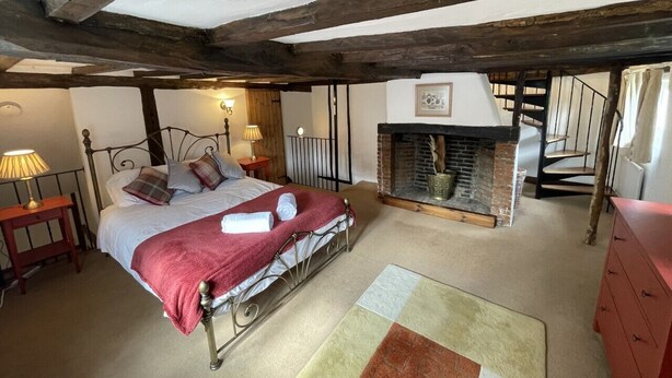 A bedroom with a metal bed frame, a fireplace, a red dresser, and a wooden ceiling. - Bere Cottage (Canterbury)