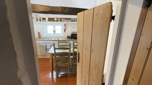 A narrow hallway with a wooden door leading to a kitchen area with a tiled floor and a dining table with chairs. - Bere Cottage (Canterbury)