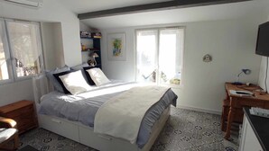 A bedroom with a bed, a desk, a chair, and a window. - Charming stone-built 2-person apartment, in a quiet location with pool access.  (Lorgues)