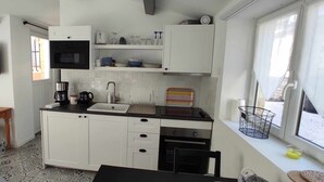 A compact kitchen with white cabinets, a black countertop, a built-in oven, and a window with a view. - Charming stone-built 2-person apartment, in a quiet location with pool access.  (Lorgues)