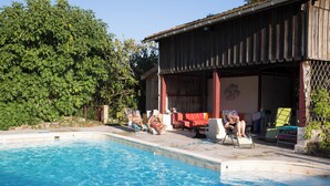 A swimming pool with a wooden deck and a covered area with chairs and a table. - Beautiful stone house with swimming pool in a protected nature setting (Pondaurat)