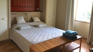 A bedroom with a bed, a wooden nightstand, a red accent wall, and a window with curtains. - Beautiful stone house with swimming pool in a protected nature setting (Pondaurat)