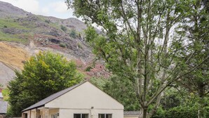 A single-story building with a sloped roof, surrounded by a wooden fence, set against a backdrop of hills and trees. - Awel Y Berwyn (Oswestry)