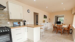 A modern kitchen with white cabinets, a black stove, and a wooden countertop. There is a dining area with a round table and wooden chairs. - Awel Y Berwyn (Oswestry)