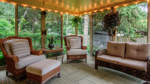 A sunroom with wicker furniture, large windows, and hanging plants. - Warm & light-filled home with gym (Ann Arbor)