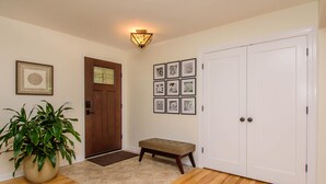 A hallway with a wooden floor, a potted plant, a bench, a door, and a wall with framed pictures. - Warm & light-filled home with gym (Ann Arbor)