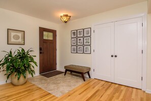 A hallway with a wooden floor, a potted plant, a bench, a door, and a wall with framed pictures. - Warm & light-filled home with gym (Ann Arbor)