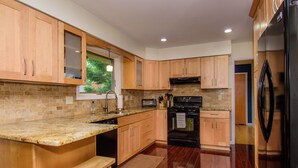 A modern kitchen with wooden cabinets, a granite countertop, a built-in oven, and a stainless steel refrigerator. - Warm & light-filled home with gym (Ann Arbor)
