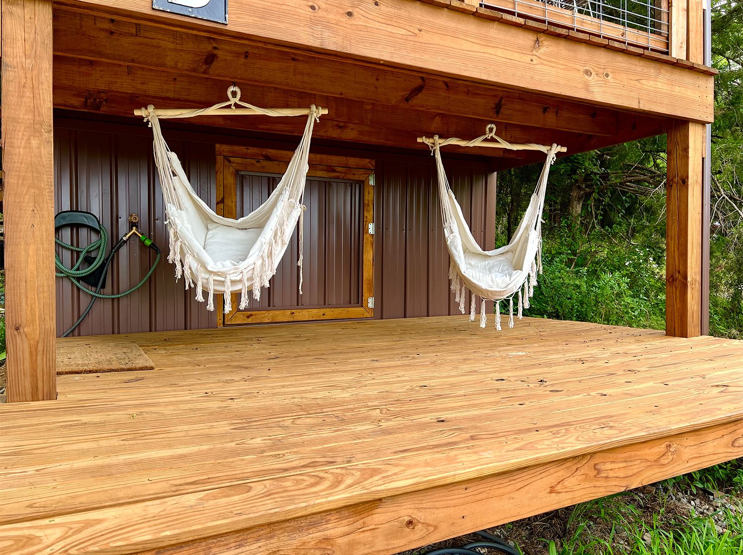 A wooden deck with two white hammocks hanging from the ceiling.