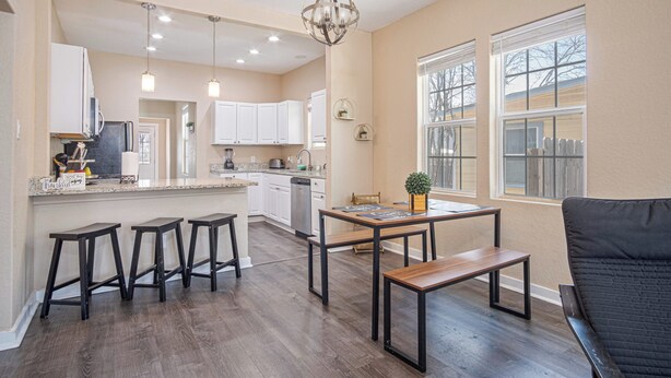 Una cocina moderna con armarios blancos, una zona de comedor con mesa y taburetes de madera, y un ventanal con vistas al exterior.