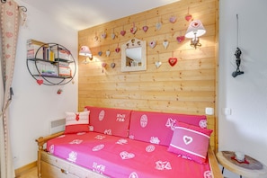 Ein gemütliches Schlafzimmer mit einem hölzernen Kopfende, einem Bücherregal, einem Spiegel und herzförmigen Dekorationen.