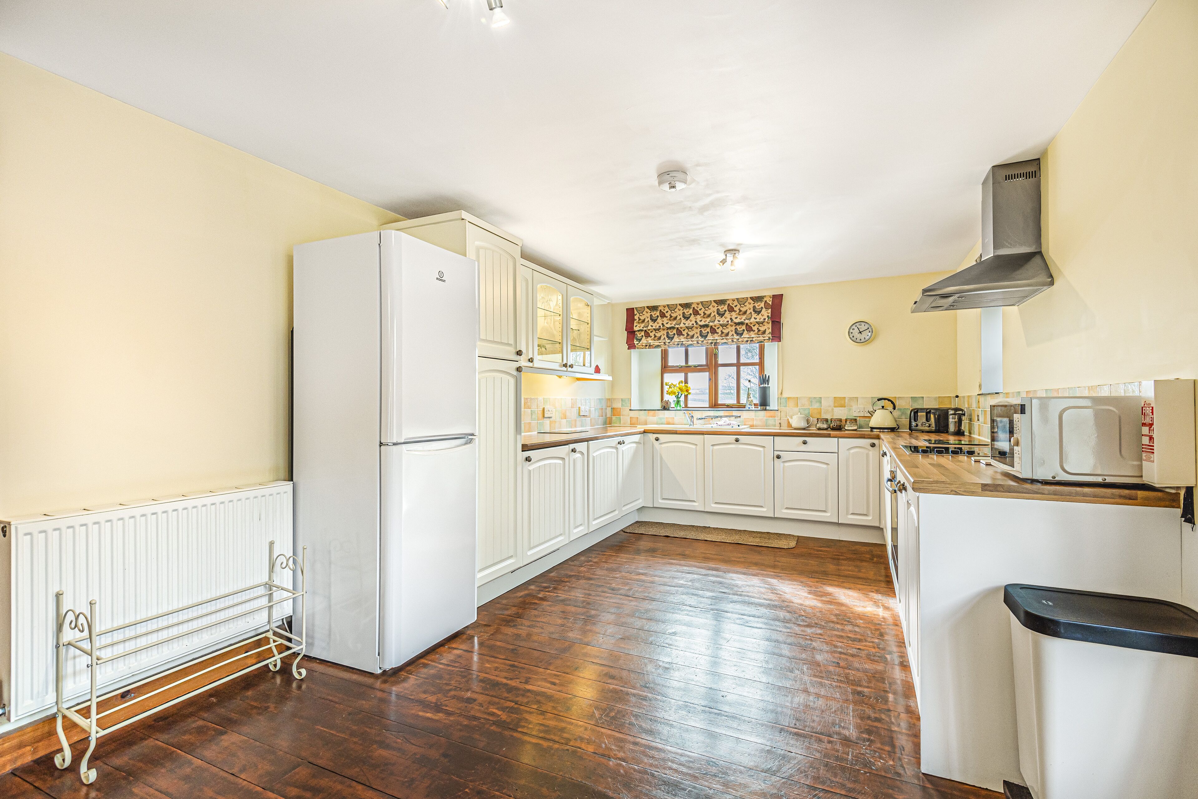A kitchen with white cabinets, a wooden floor, a white refrigerator, a microwave, and a window with a curtain.