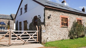 A stone building with a white facade, a wooden gate, and a grassy area in front. - Spacious and Characterful 3 bedroom Detached Barn Conversion close to coast. (Hartland)
