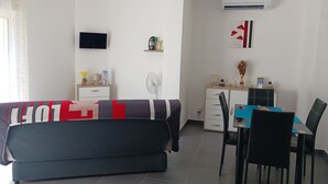 Una sala de estar moderna con un sofá, una mesa de comedor con sillas, un televisor y un ventilador.