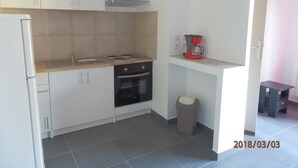 Cocina compacta con armarios blancos, estufa, horno y cafetera sobre una encimera.