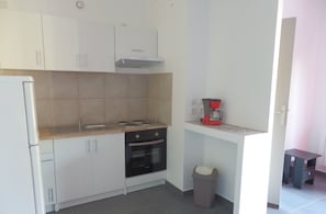 A compact kitchen with white cabinets, a stove, oven, and a coffee maker on a countertop.