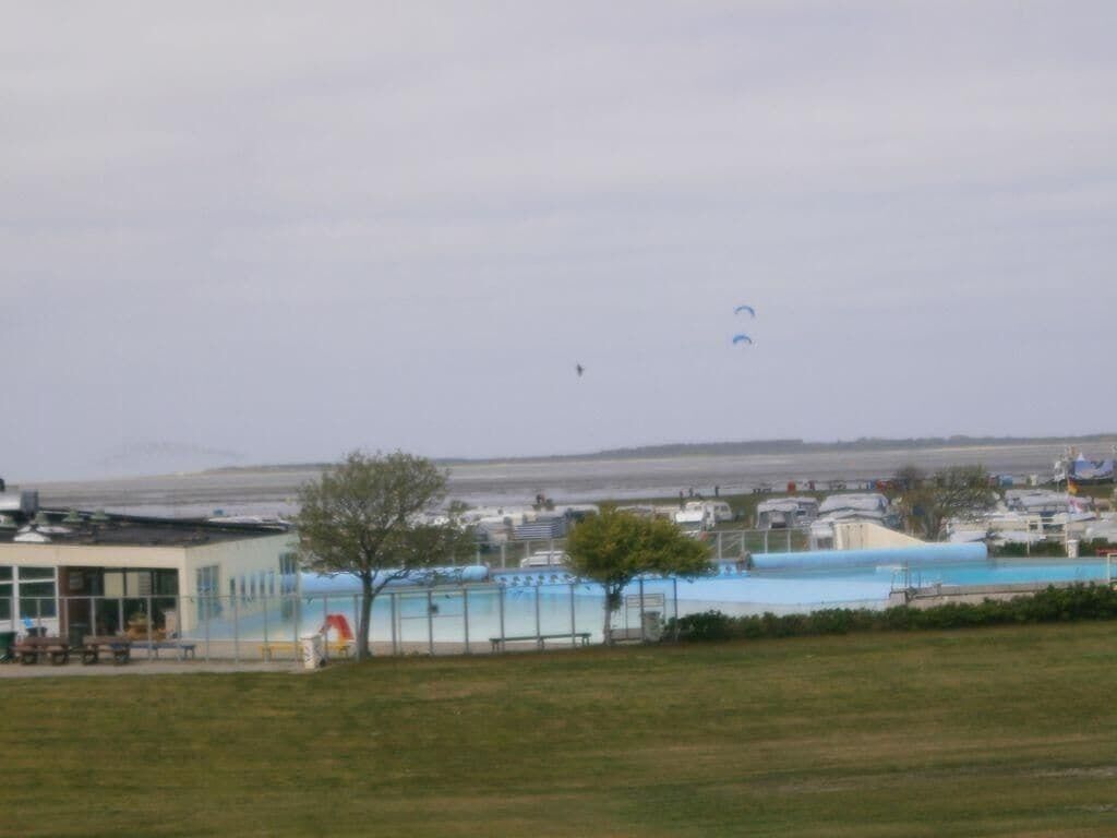 A building with a swimming pool, a fenced area, and a grassy field.