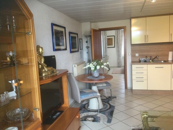 A dining area with a table and chairs, a kitchen with cabinets, and a statue on a shelf.