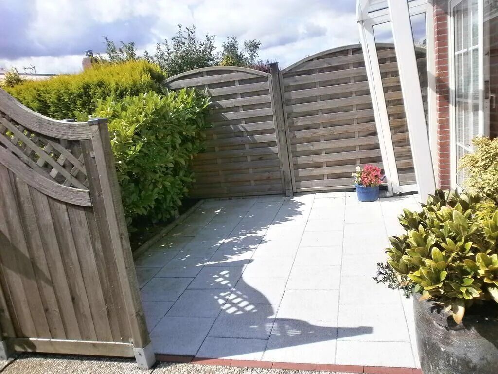 A paved patio with a wooden gate, a potted plant, and a brick wall.