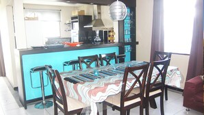 A dining area with a large table, chairs, and a kitchen in the background.