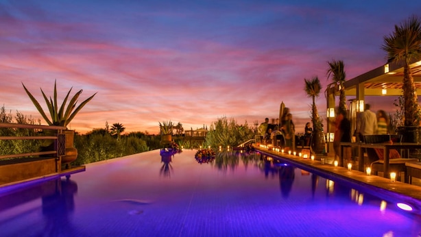 A pool with a sunset view, surrounded by palm trees and outdoor seating. - Villa Le Clos des Oliviers (Marrakech Alentours)