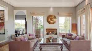 A spacious living room with a fireplace, two sofas, a coffee table, and large windows. - Villa Le Clos des Oliviers (Marrakech Alentours)