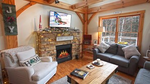 A cozy living room with a fireplace, a television, and a couch. - Secluded, Cozy Cabin on 10 Acres of Woods ~16 mi to Slopes & Pet Friendly! (Whitingham)