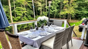 An outdoor dining area with a table set for six, surrounded by wicker chairs with cushions. - Secluded, Cozy Cabin on 10 Acres of Woods ~16 mi to Slopes & Pet Friendly! (Whitingham)